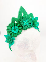 Green glitter floral headband with green glitter tiara. Flowers have layers of petals and diamonte centres on a white glitter display head