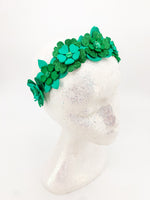 Green glitter floral headband with layers of petals and diamonte centres on a white glitter display head