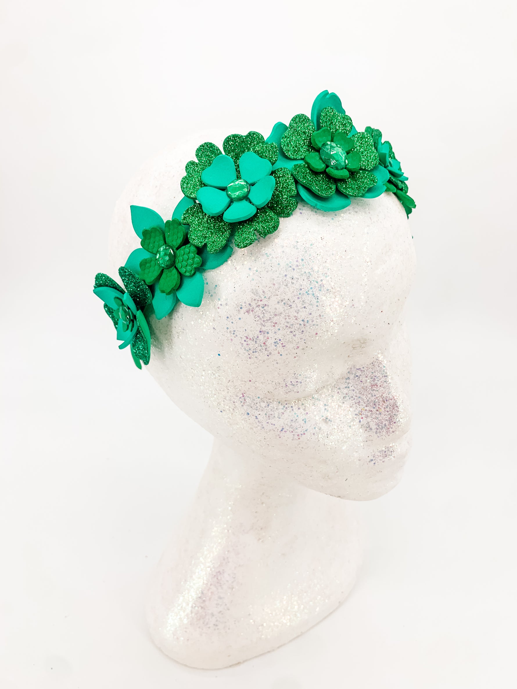 Green glitter floral headband with layers of petals and diamonte centres on a white glitter display head