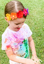 Child wearing a colorful tie-dye shirt and headband with flowers on a grassy background