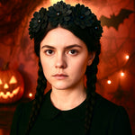 Teen girl looks like Wednesday Addams with long black plaits wearing a black flower headband with Halloween decorations in the background