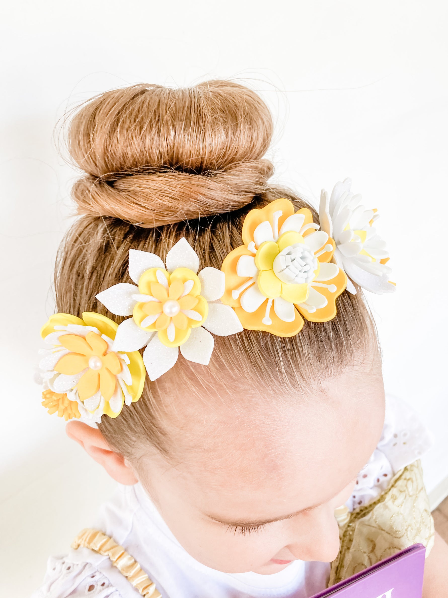Child with a floral headband featuring yellow and white flowers on a plain background
