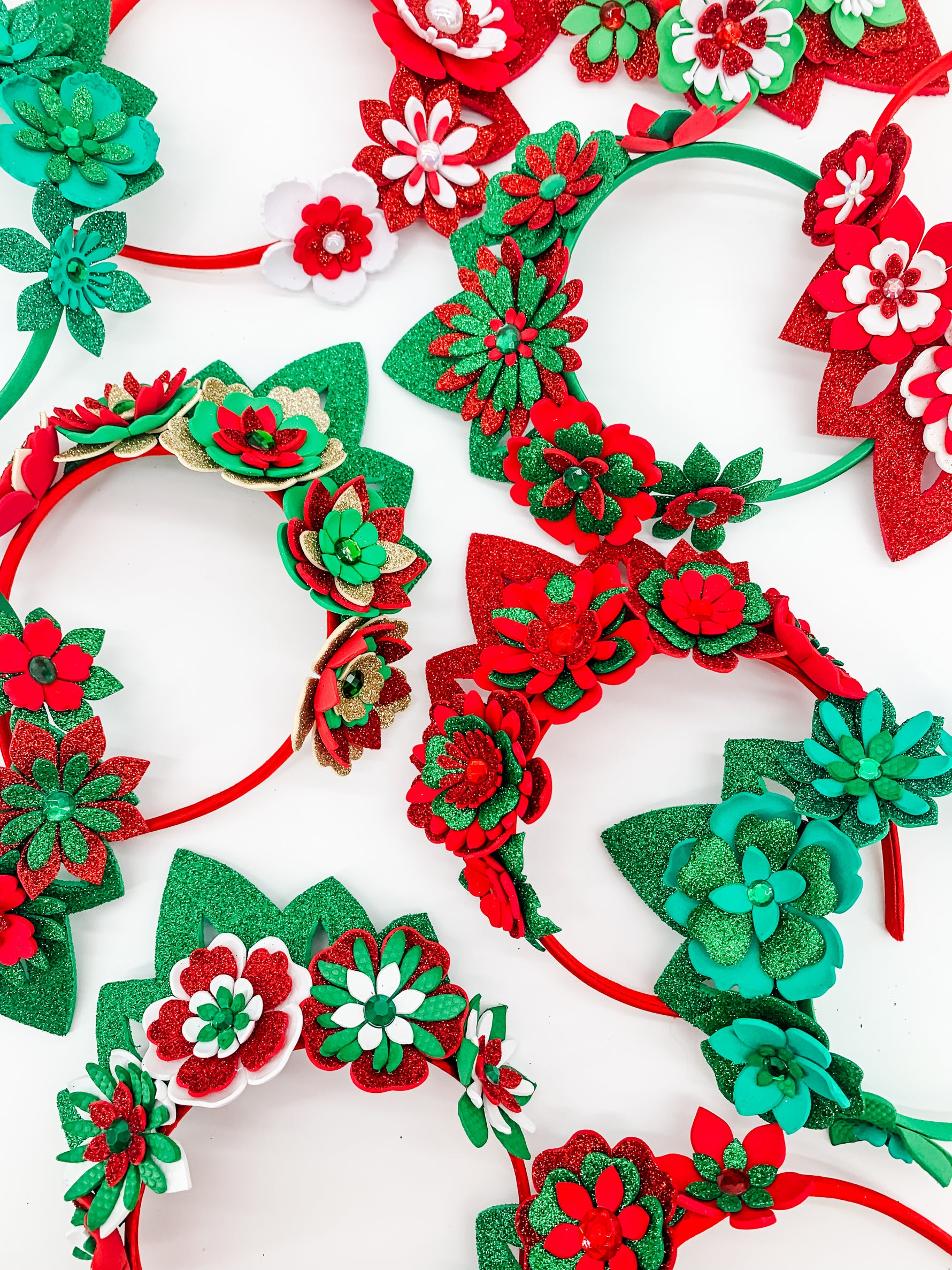 A variety of Green, red and gold glitter floral headbands with green or red glitter tiaras. Flowers have layers of petals and diamonte centres. 