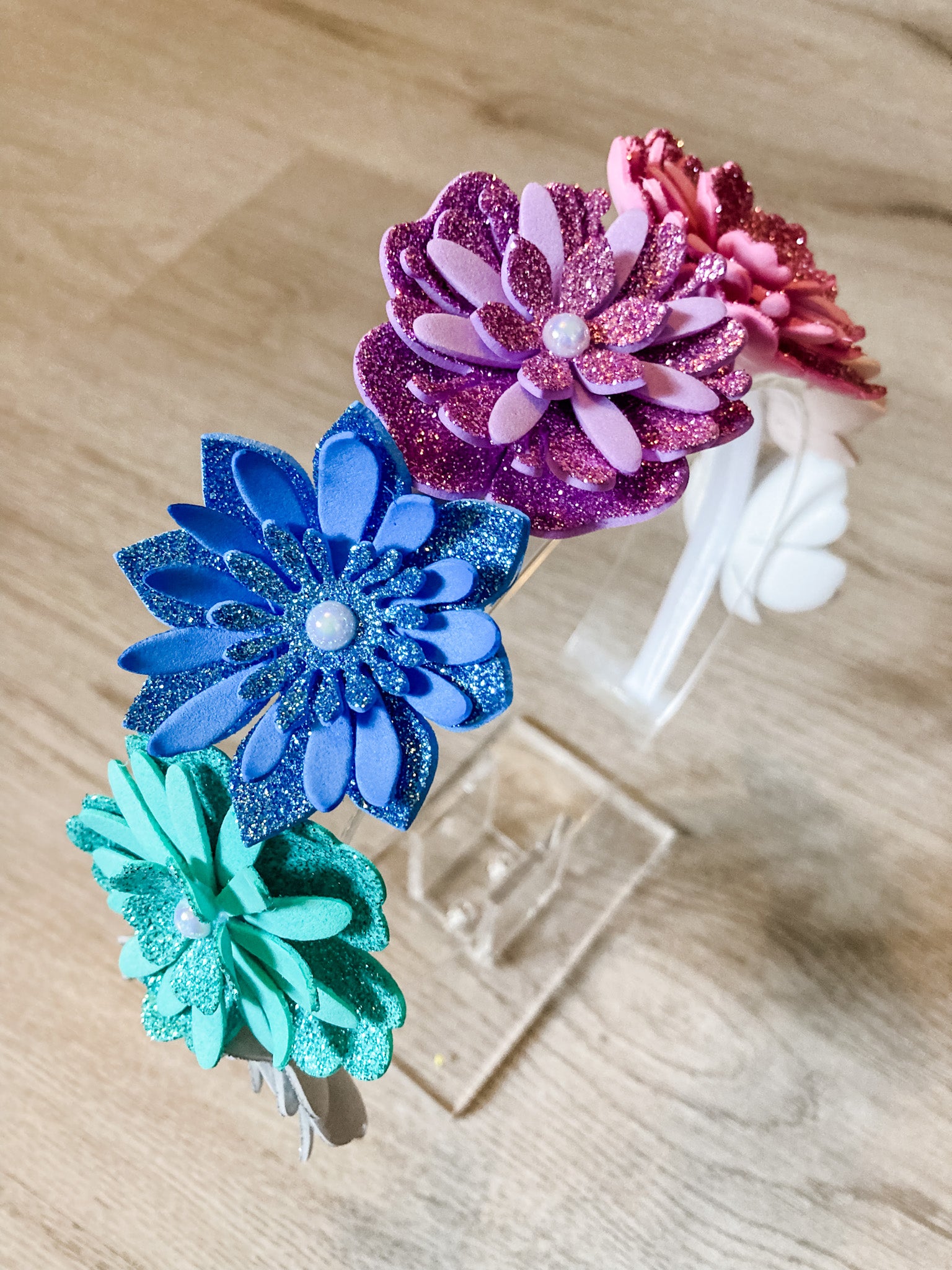 Three glittery flower hair clips in blue, pink, and green on a wooden surface.