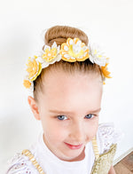Young girl wearing a floral headband with yellow and white flowers on a plain background