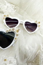 Heart-shaped sunglasses with floral embellishments on a white fabric background