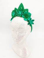 Green glitter floral headband with green glitter tiara. Flowers have layers of petals and diamonte centres on a white glitter display head