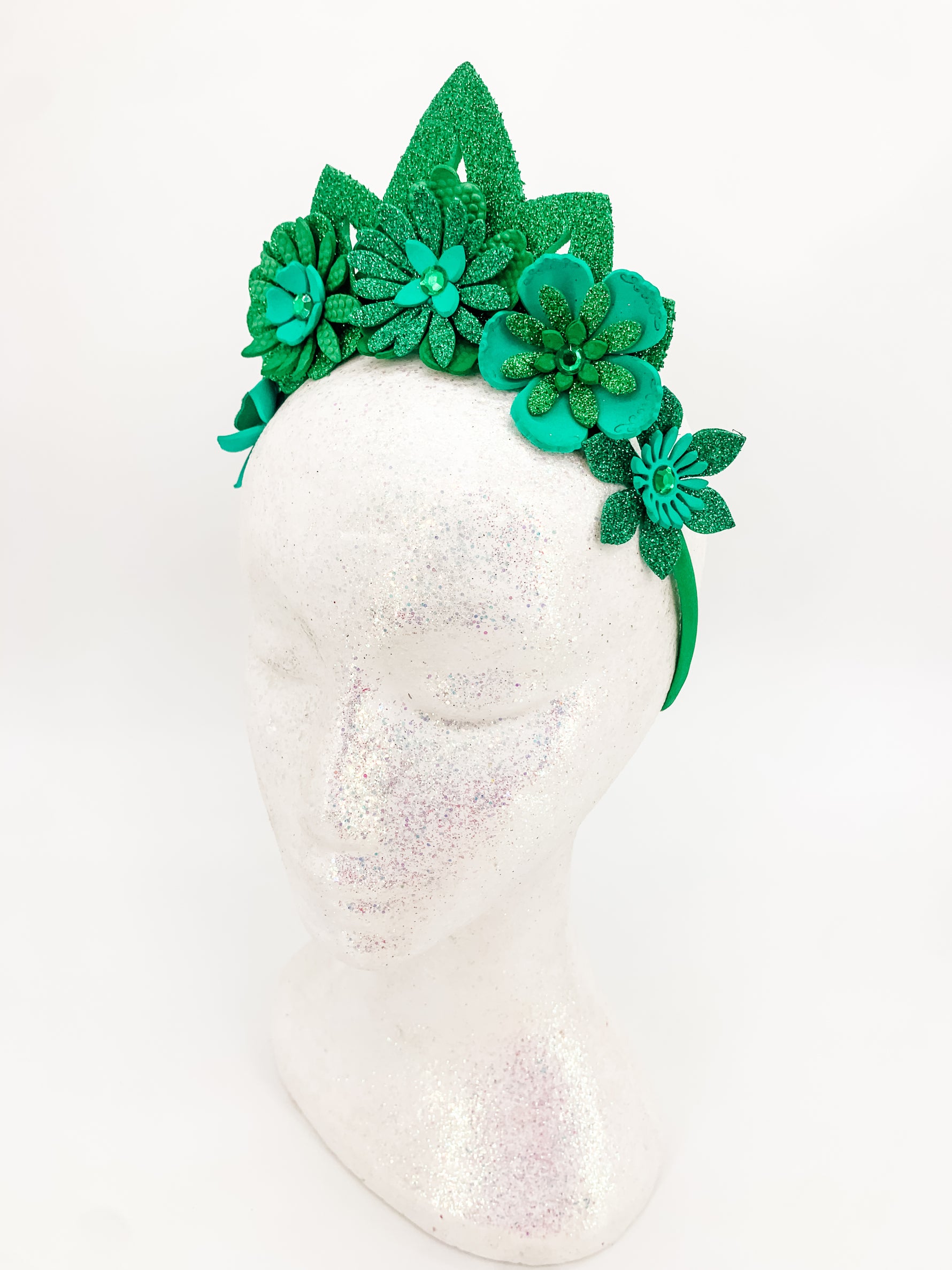 Green glitter floral headband with green glitter tiara. Flowers have layers of petals and diamonte centres on a white glitter display head