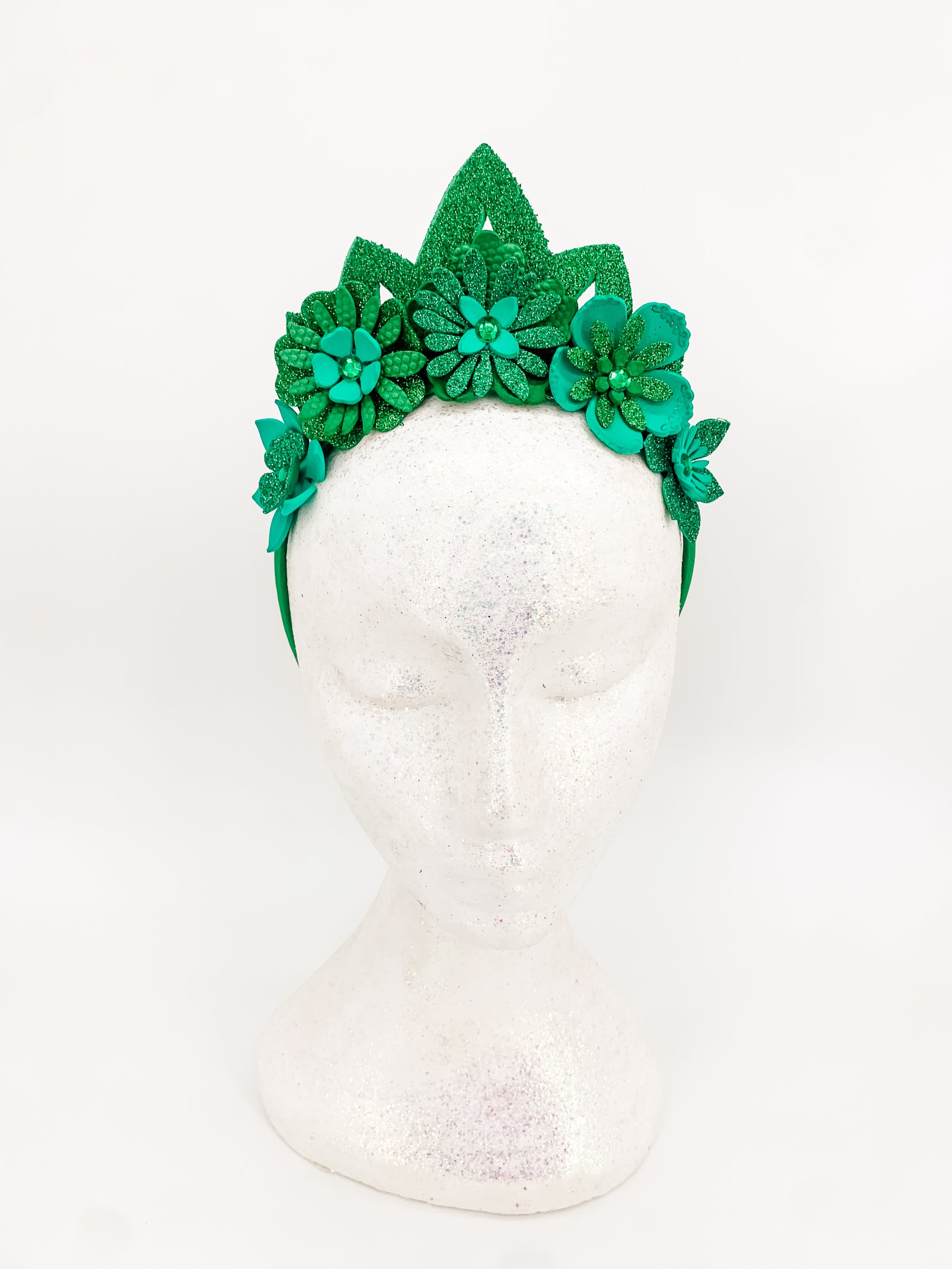 Green glitter floral headband with green glitter tiara. Flowers have layers of petals and diamonte centres on a white glitter display head