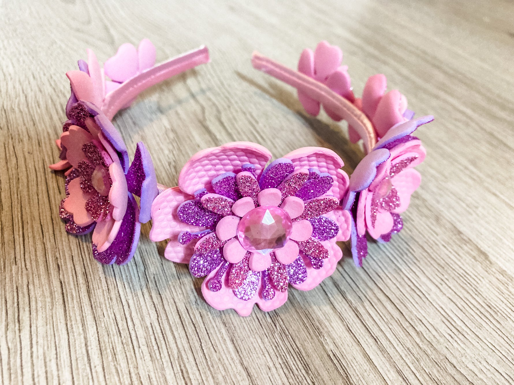 Pink and purple floral headband with glitter on a wooden surface