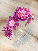 Two pink and purple flower-shaped hair accessories on a wooden surface.