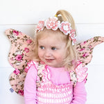 Child wearing pink floral fairy wings and a matching outfit on a white background