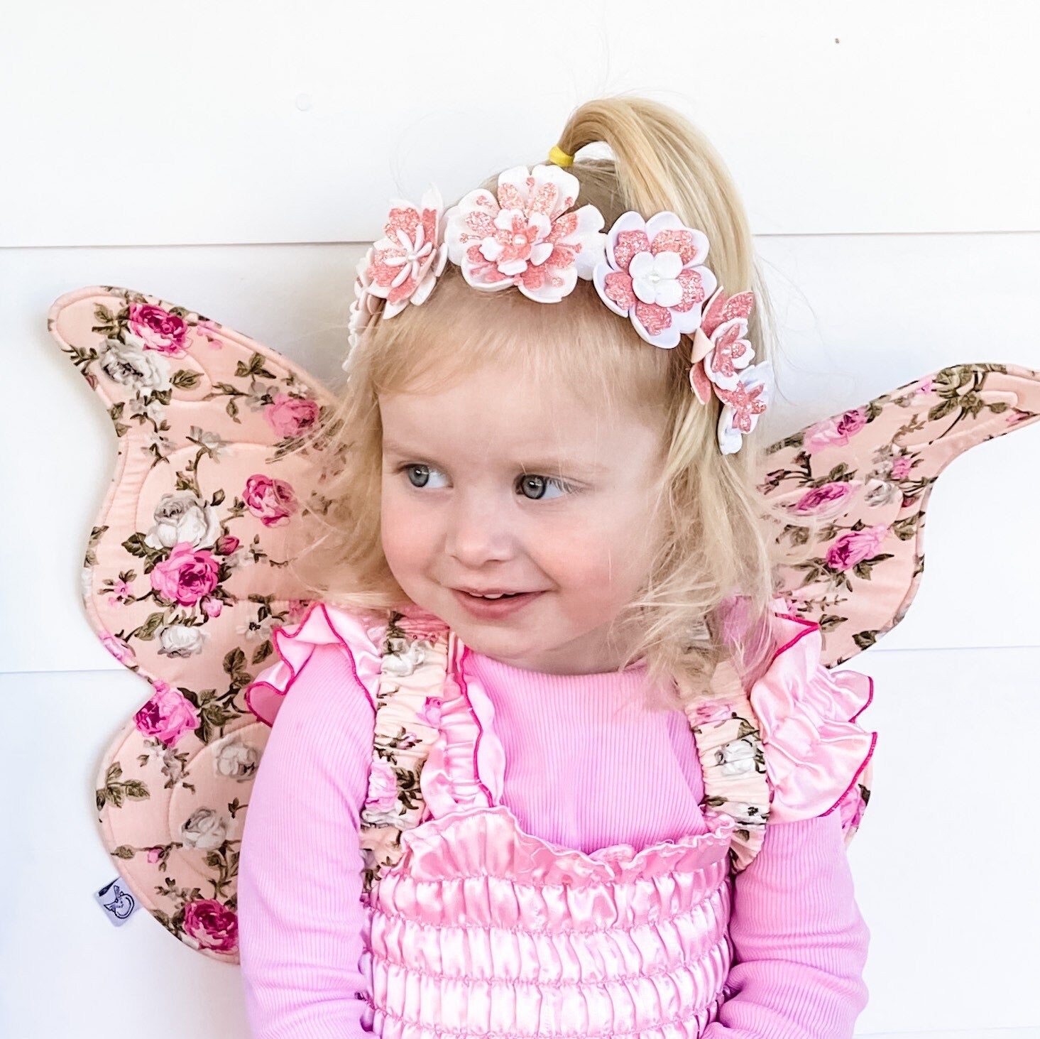 Child wearing pink floral fairy wings and a matching outfit on a white background