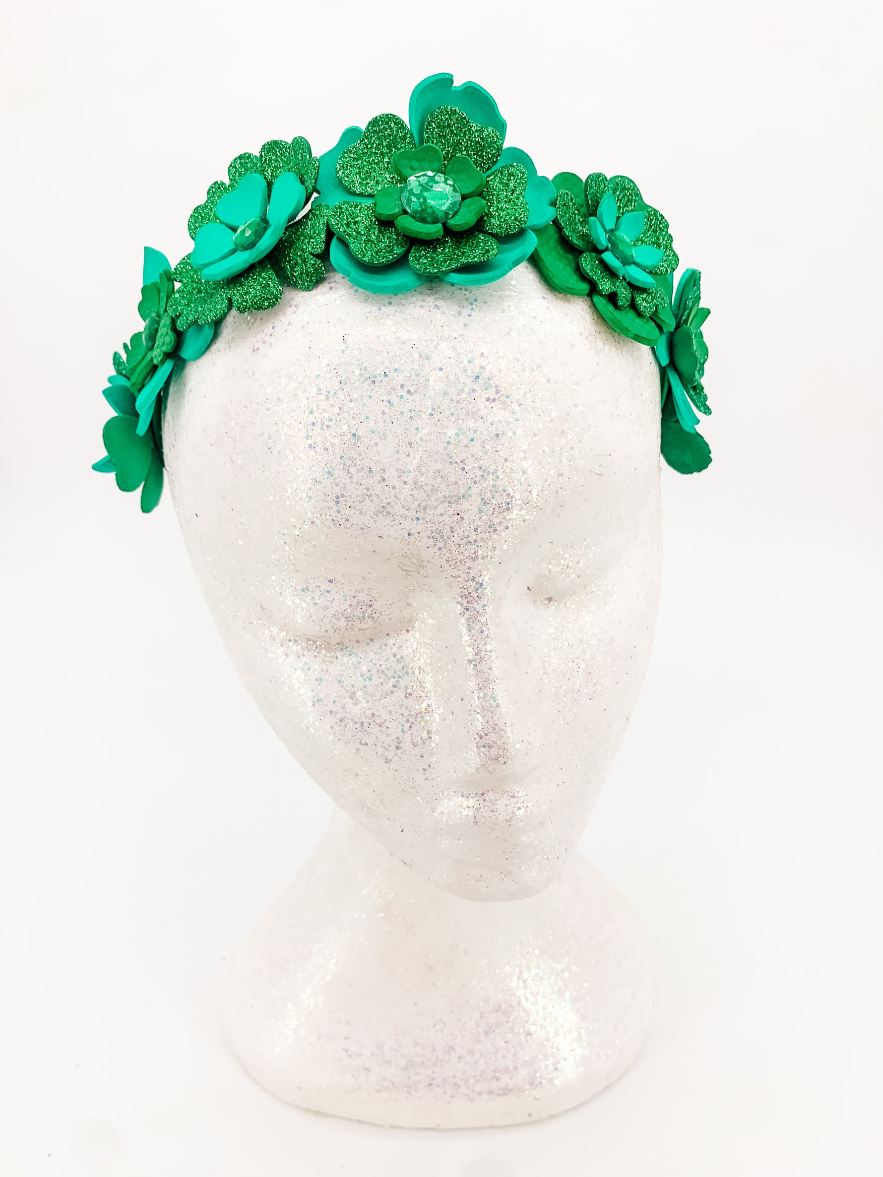 Green glitter floral headband with layers of petals and diamonte centres on a white glitter display head