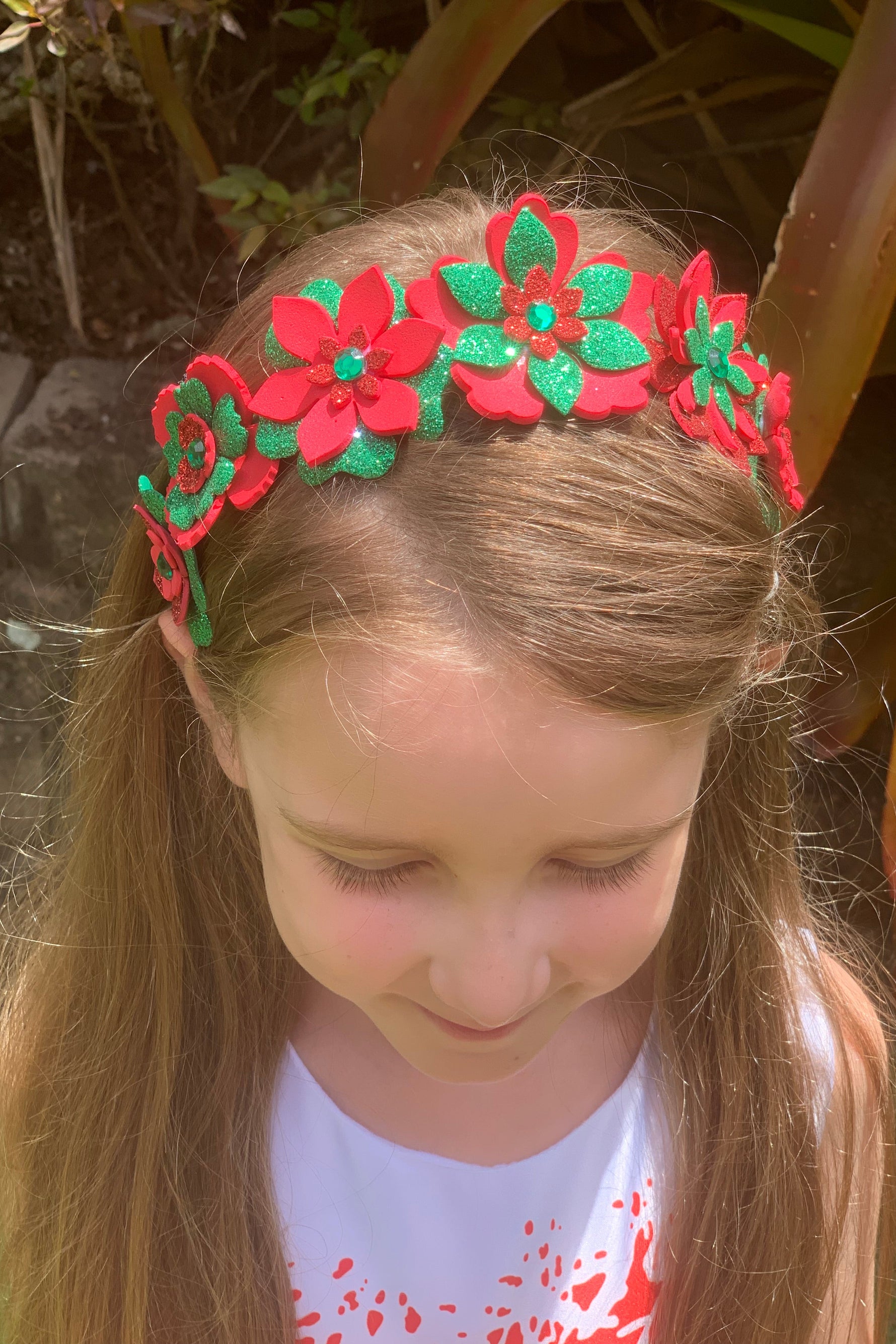 Close-up of a person wearing a red and green floral headband outdoors.