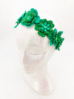 Green glitter floral headband with layers of petals and diamonte centres on a white glitter display head