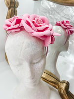 Baby pink roses and buds made of soft foam shaped across a headband fascinator. Displayed on a glitter white mannequin head with an ornate gold mirror behind. 