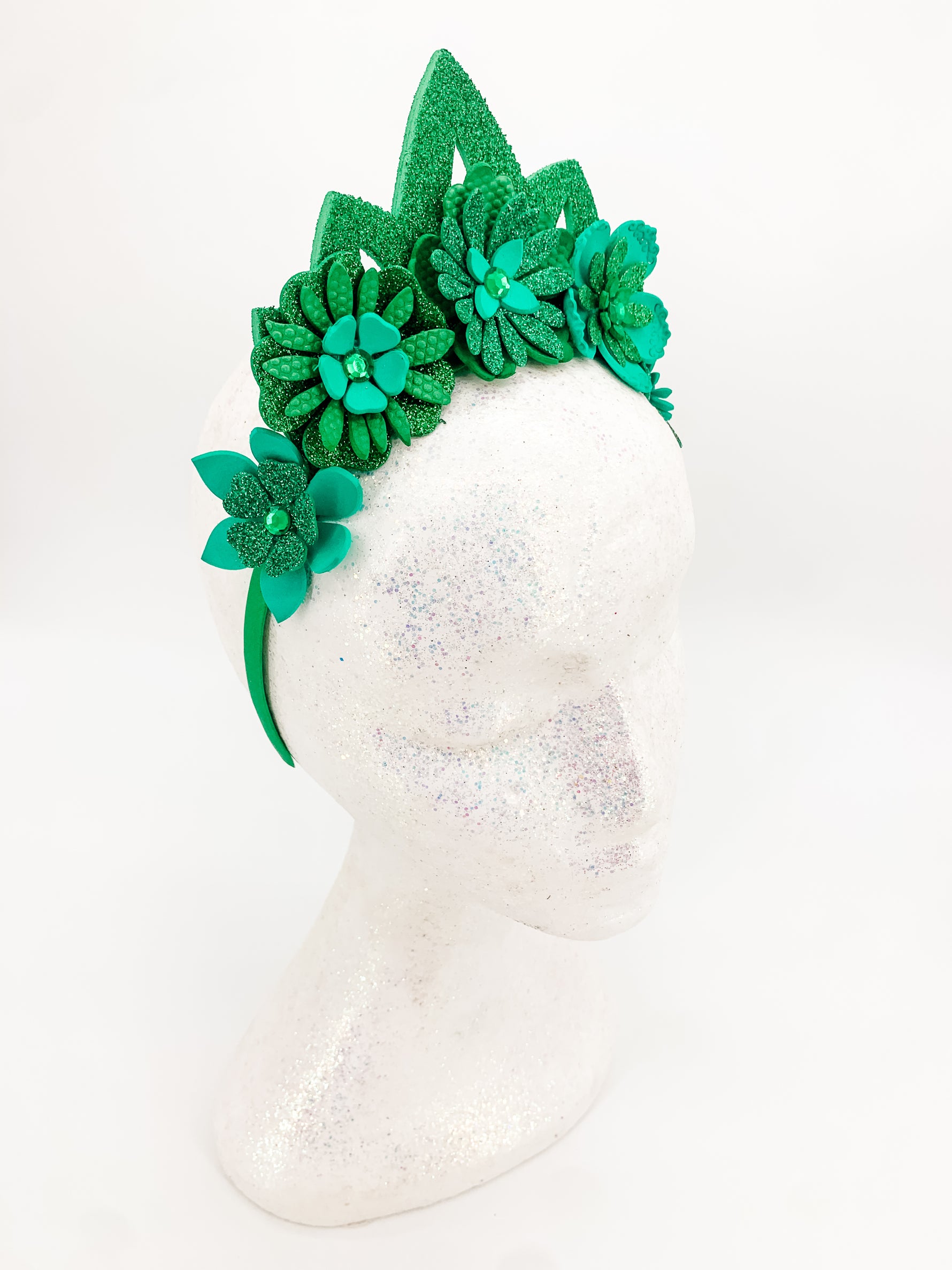 Green glitter floral headband with green glitter tiara. Flowers have layers of petals and diamonte centres on a white glitter display head