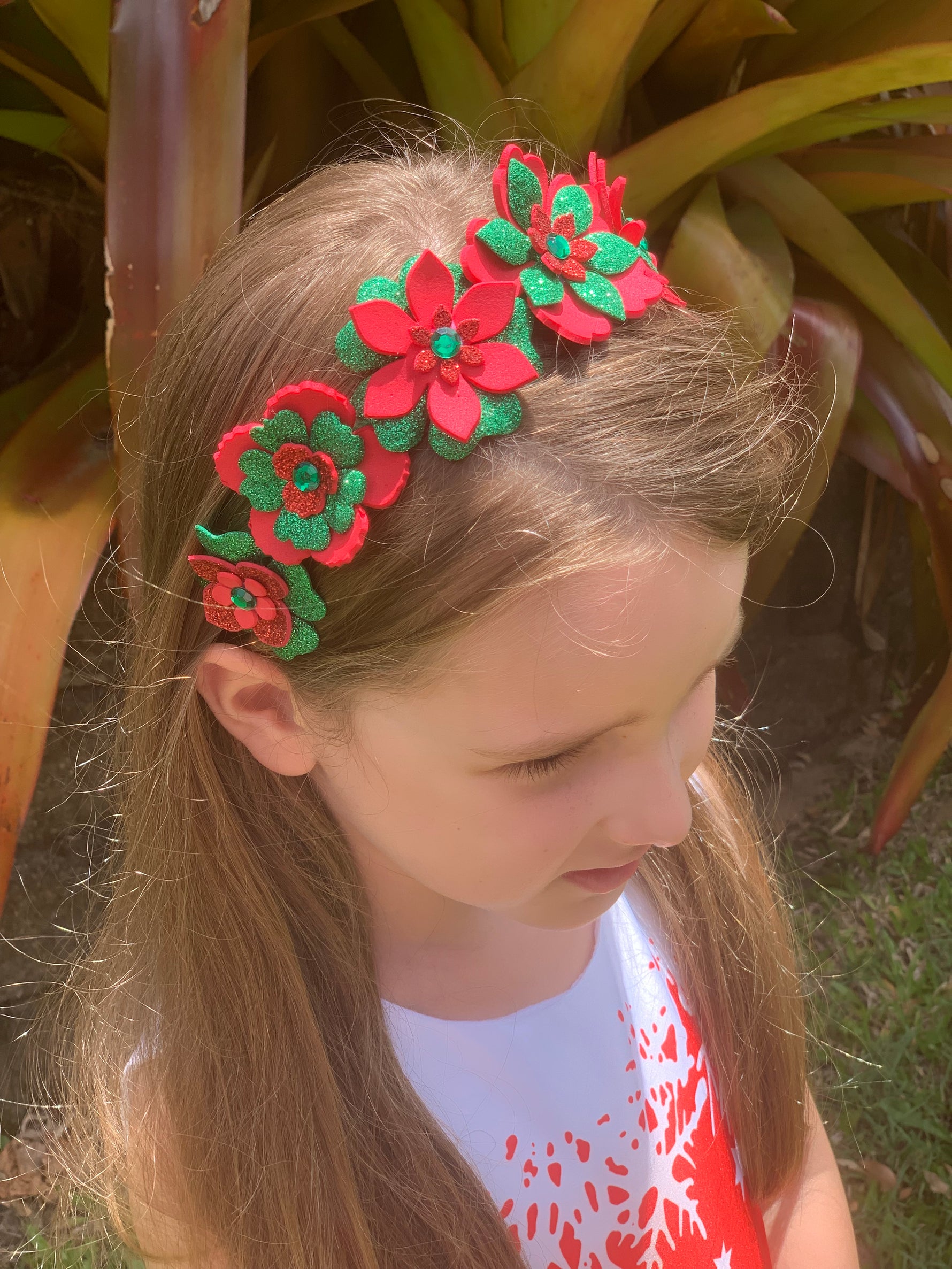 Child wearing a floral headband with red and green flowers outdoors.