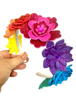 Colorful flower-shaped hair accessories held by a hand against a white background.