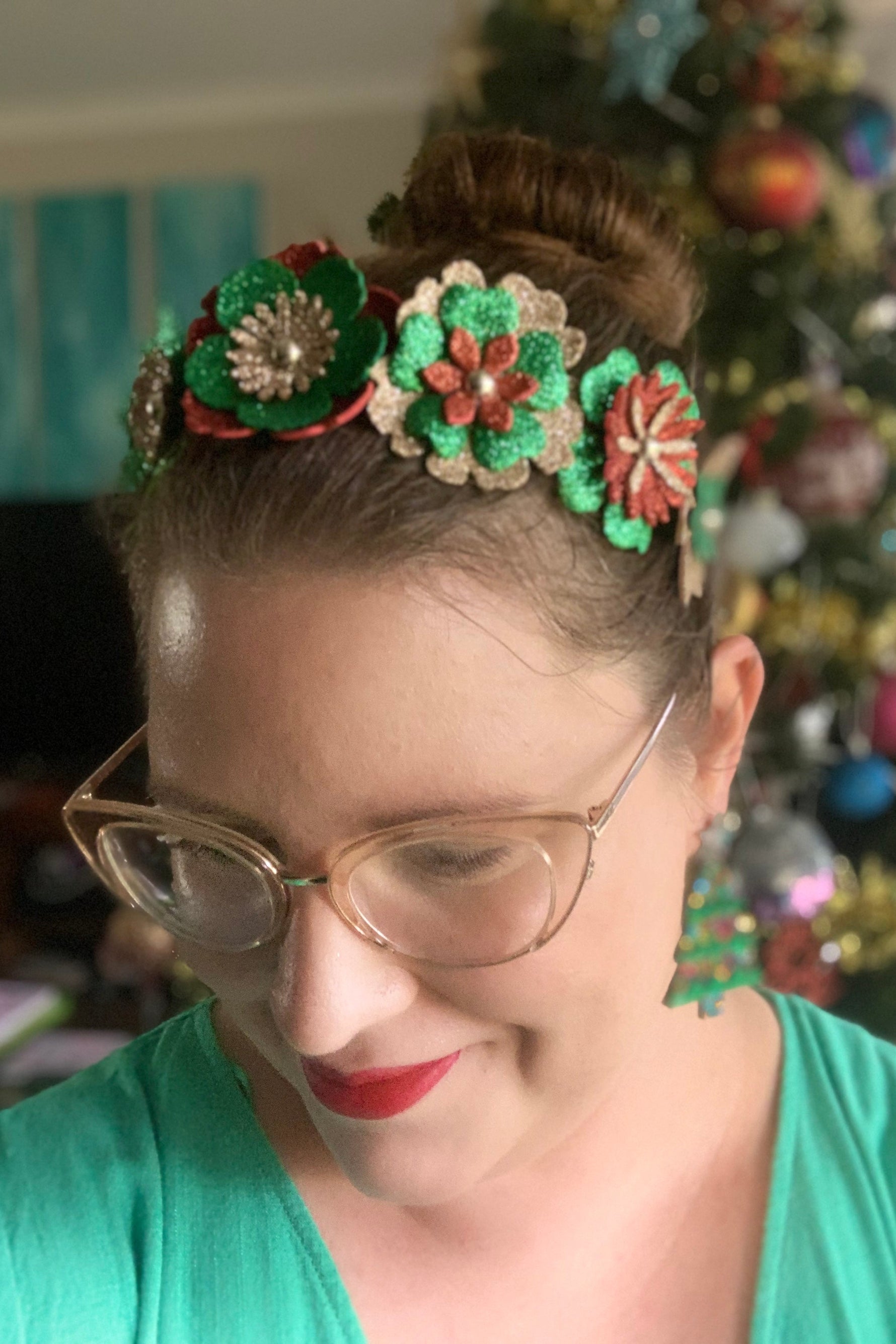 Person wearing a decorative headband with red, green and gold flowers in front of a Christmas tree