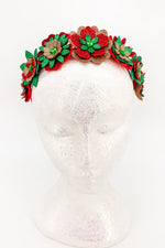 Decorative headband with red, gold and green flowers on a mannequin head against a white background 